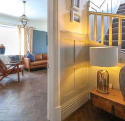 A hallway with a wooden bench lamp and vase next to carpeted stairs and a living room with armchair couch and window at The Manor House Skerry Vore Bryn Pydew near Llandudno Junction