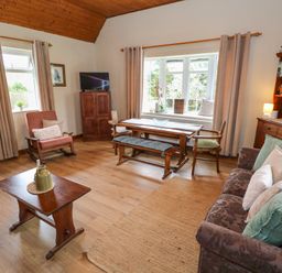 A living room with wooden furniture a sofa with cushions a coffee table a TV on a cabinet and a dining table with chairs and a bench at Aggrafard in Oughterard County Galway
