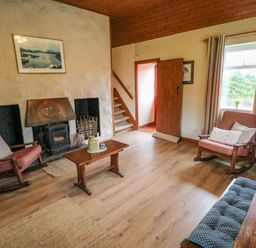 A living room with wooden rocking chairs a wooden coffee table a stove fireplace staircase and a window with curtains at Aggrafard in Oughterard County Galway