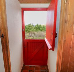 An interior view of a small vestibule with a red stable door partially open showing greenery outside at Aggrafard in Oughterard County Galway