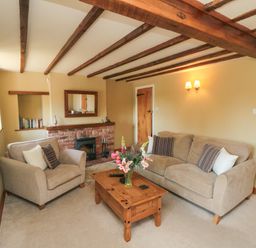 A living room with a sofa an armchair a wooden coffee table a fireplace and a wall-mounted television at Tillers Cottage in Ebberston