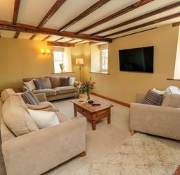 A living room with beige sofas a wooden coffee table a wall-mounted TV and exposed wooden ceiling beams at Tillers Cottage in Ebberston