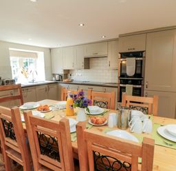 A kitchen with wooden dining table set for breakfast with plates croissants and juice at Tillers Cottage in Ebberston