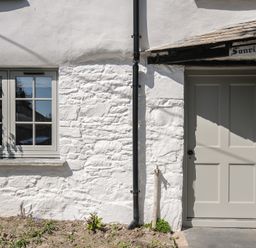 Exterior of a white stone cottage with a window and a door with a black drainpipe between them at Sunrise Cottage St Kew Highway near Wadebridge