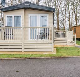 A caravan with a beige deck and two chairs outside on a paved area surrounded by grass at The Mermaid A04 in Par