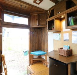 A wooden interior room with a small kitchenette, a fridge, shelves, a cork board with papers, and a door leading outside at Daisy Cow Shed 1 Easton near Campsea Ashe