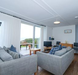 A living room with two grey sofas a small wooden coffee table a TV on a stand and sliding glass doors leading to a deck at Ael Y Don in Llandanwg