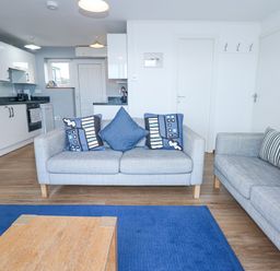 A living room with two sofas and a wooden coffee table next to an open kitchen at Ael Y Don in Llandanwg