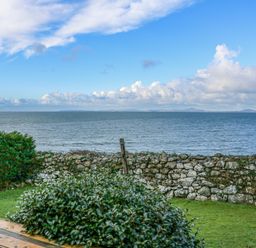 A view of the sea with clouds a stone wall bushes and grass at Ael Y Don in Llandanwg