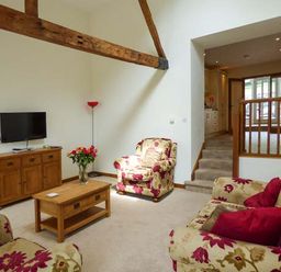 A living room with floral armchairs a wooden TV stand with a television a wooden coffee table and a floor lamp at Ghyll Bank Barn in Staveley near Windermere