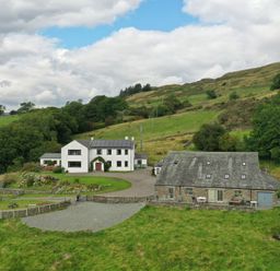 A white house and a stone barn in a rural hillside setting with green fields at Ghyll Bank Barn in Staveley near Windermere