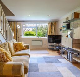 A living room with a striped sofa cushions a window with curtains a television and shelving unit at 50 Fernhill Heights in Charmouth