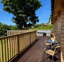 A wooden deck with outdoor seating and a table with two chairs at Northwood Lodge in Llanbedrog