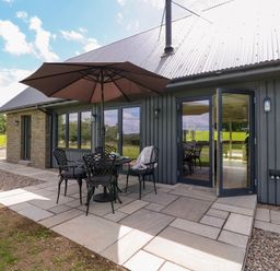 An outdoor patio with a table umbrella and chairs next to a building with glass doors at Strawberry Cottage Wester Essendy near Dunkeld