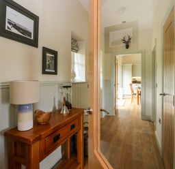 A hallway with a wooden console table holding a lamp and decor leading to a kitchen with cabinets and a dining table at Strawberry Cottage Wester Essendy near Dunkeld