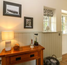 A wooden console table with a lamp a wooden bowl a hand bell and a glass vase in a room with two windows a basket on the floor at Strawberry Cottage Wester Essendy near Dunkeld