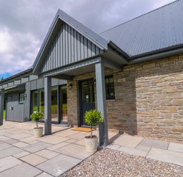 Front entrance of a house with stone and vertical wood panel exterior walls and potted plants at Bramble Cottage Wester Essendy near Dunkeld