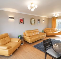 A living room with three yellow sofas a round dining table and chairs a rug wall clock and posters at 315 Filey Road Scarborough