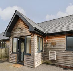 A wooden cabin with a black door and windows and a small fenced area at Caban Dulas in Rhayader