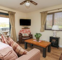 A living room with a sofa and armchairs a wooden coffee table a TV mounted on the wall and a window with blinds at Caban Dulas in Rhayader