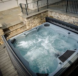 An outdoor hot tub with bubbling water next to stone walls and metal railings at Pen-y-Ghent in Kirkby Lonsdale