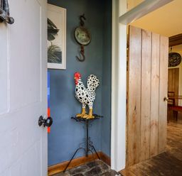 A corner with a decorative rooster statue on a metal stand next to an open wooden door showing a dining area at Brook Farm in St Nicholas near Halesworth