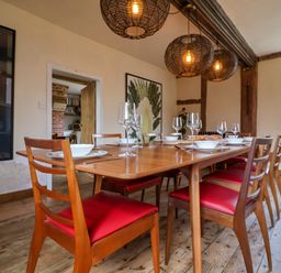 A dining room with a wooden table set for eight with red cushioned chairs and hanging wicker light fixtures at Brook Farm in St Nicholas near Halesworth