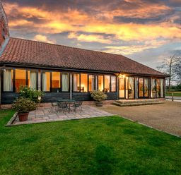 A building with tiled roof and large windows next to a patio with table and chairs and a grassy lawn at Mallard in Wheatacre