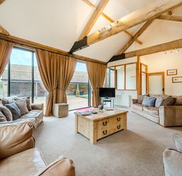 A sitting room with leather sofas a wooden coffee table and large windows with curtains at Mallard in Wheatacre