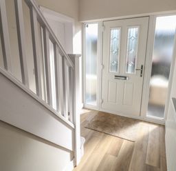 A hallway with a white front door a doormat a staircase and a radiator at Wychwood in Hook near Haverfordwest