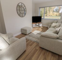 A living room with beige sofas a TV on a stand and a mirror on the wall at Wychwood in Hook near Haverfordwest