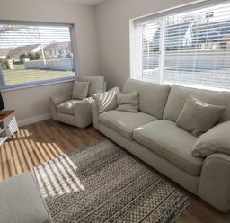 A living room with sofa armchair ottoman television and windows with blinds at Wychwood in Hook near Haverfordwest