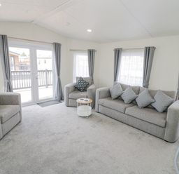 A living room with grey sofas and cushions and a small round table at Long Acres Lodge in Evesham