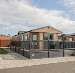 A wooden cabin with a fenced deck area and gravel driveway at Long Acres Lodge in Evesham