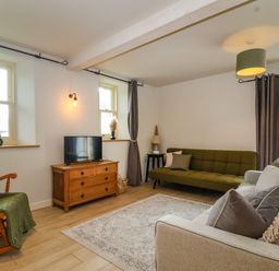 A living room with a green rocking chair a wooden TV stand with a television two sofas and large windows at 8 Rookhaye in Salisbury