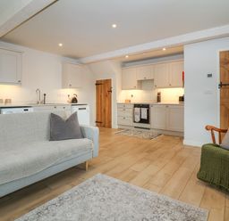 An open plan kitchen and living area with light wood flooring white cabinets and two wooden doors at 8 Rookhaye in Salisbury