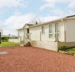 A white mobile home with glass railings on a wooden deck surrounded by lawn and red gravel at Plot 32 in High Hesket near Armathwaite