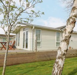 A mobile home with a wooden deck and outdoor furniture near two trees on a grass lawn at Plot 32 in High Hesket near Armathwaite