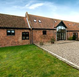 A brick building with red tiled roof windows and a gravel driveway with grass area at Coot in Wheatacre