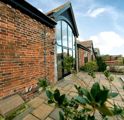 Brick building with large arched window and paved patio with plants at Coot in Wheatacre