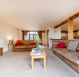 A living room with two brown leather sofas red and gray cushions a wooden coffee table with flowers and magazines and wooden beams at Coot in Wheatacre