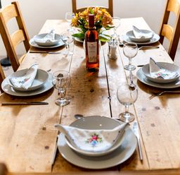 A dining table set with plates glasses cutlery napkins and a bottle of wine with flowers in the center at Coot in Wheatacre