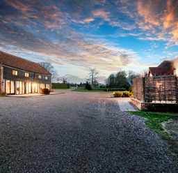 An outdoor view of buildings with lights on at dusk and a gravel driveway at Widgeon in Wheatacre
