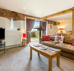 A living room with a brown leather sofa and coffee table facing a television at Widgeon in Wheatacre