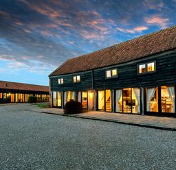 A courtyard with two rustic buildings with large windows and tiled roofs under a cloudy sky at Woodcock in Wheatacre
