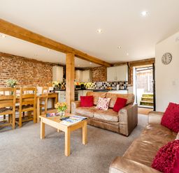 A living room and kitchen area with brown leather sofas and wooden dining table at Woodcock in Wheatacre