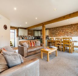 An open living area with two brown leather sofas wooden coffee and dining tables exposed brick walls and kitchen cabinets at Snipe in Wheatacre