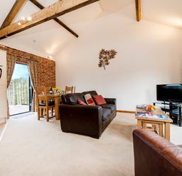 A living room with a wooden dining table and chairs a brown leather sofa a coffee table with fruit and magazines a television and exposed wooden beams at Pheasant in Wheatacre