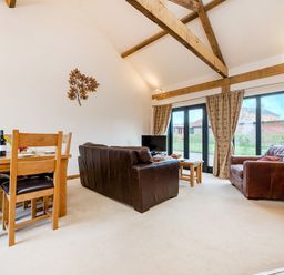 A living room with wooden dining table chairs brown leather sofas wall art and large windows with curtains at Pheasant in Wheatacre