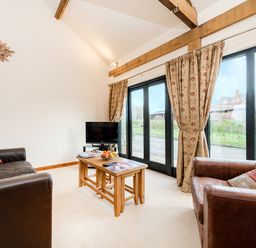 A living room with two leather armchairs a wooden coffee table a small television and large glass doors with curtains at Pheasant in Wheatacre